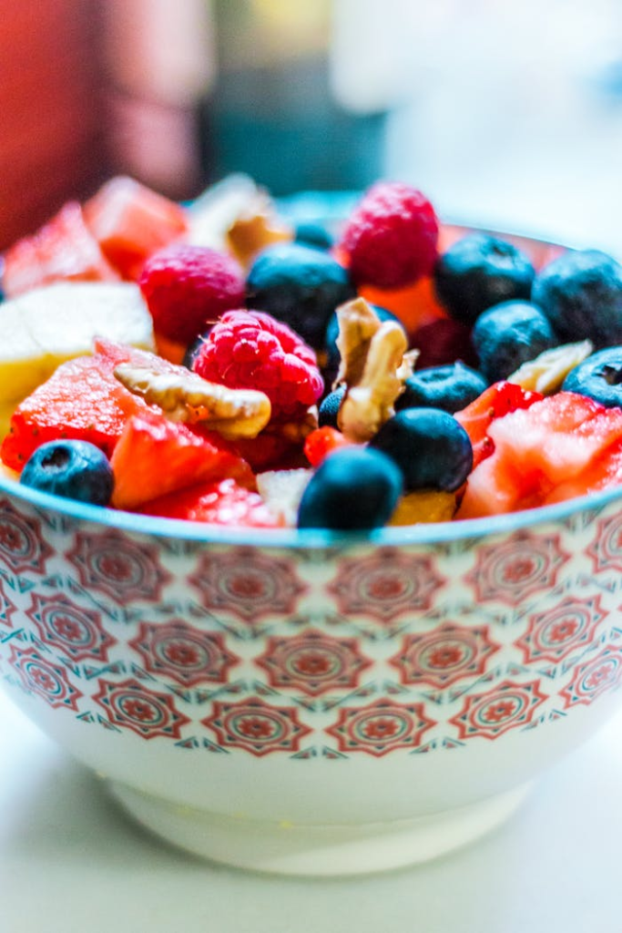 Colorful fruit salad in a decorative bowl with fresh berries and nuts, perfect for a healthy and organic snack.